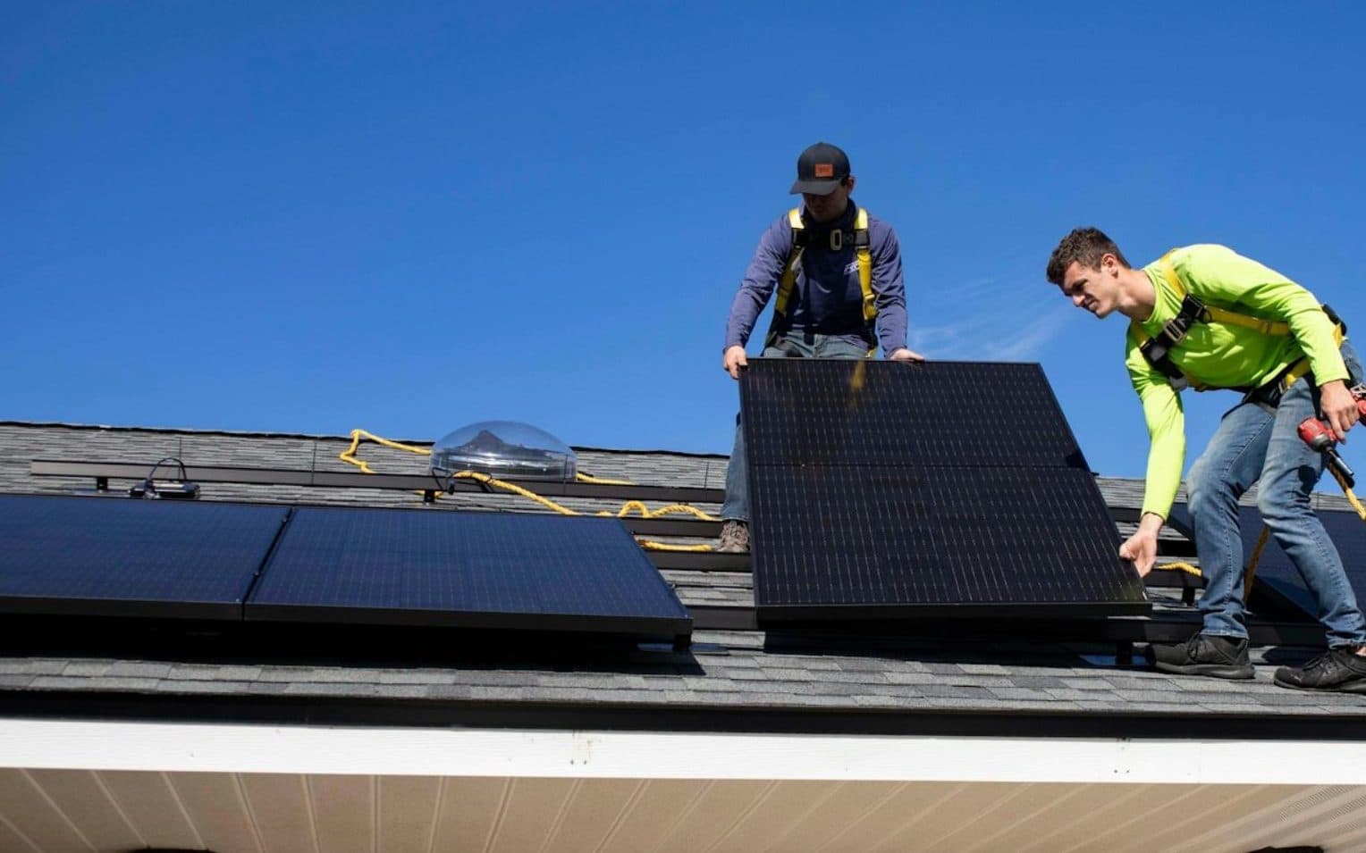 Two technicians in safety harnesses installing a solar panel on a house roof